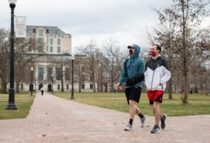 Two students wear masks as they walk across the oval with Thompson Library in the background.