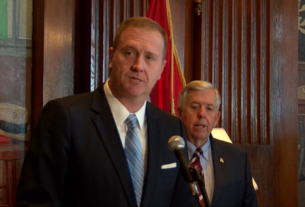 Missouri Attorney General Eric Schmitt speaks at a news conference with Gov. Mike Parson in the background.